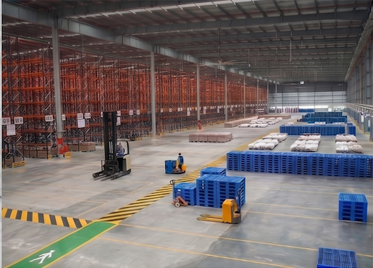 Expansive Srinivasa warehouse with high-density orange racking, blue pallets and a forklift in operation